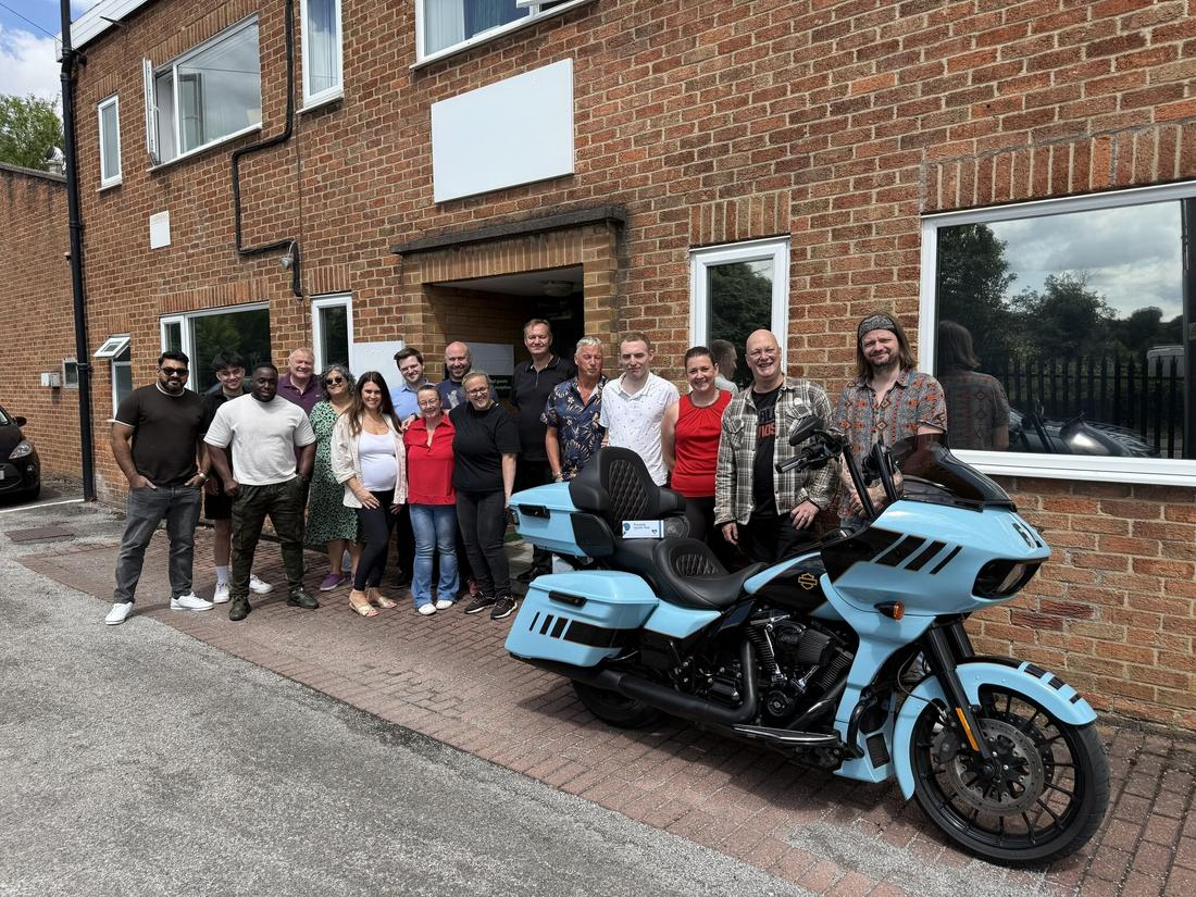 Group of people standing next to a blue motorcycle in front of a brick building.
